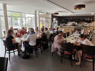 Eine Gruppe von Menschen sitzt an einem Tisch in einem hellen, modernen Restaurant. Sie scheinen miteinander zu sprechen und zu essen.