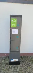 Ein Metallkasten mit mehreren Fächern, der als E-Bikeladestation dient. Eine grüne Beschilderung deutet auf die Nutzung hin.