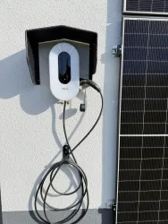 Eine Ladestation für Elektroautos ist an der Wand montiert. Daneben befindet sich ein Solarpanel, das für nachhaltige Energie sorgt.