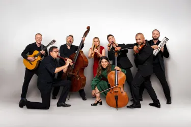 Eine Gruppe von Musikern posiert zusammen für ein Foto. Sie spielen verschiedene Instrumente und sind in festlicher Kleidung.