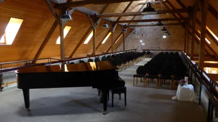 Ein eleganter Konzertsaal mit einem großen Flügel und zahlreichen Sitzplätzen. Die Holzbalkendecke verleiht dem Raum eine warme Atmosphäre.