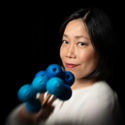 Eine Frau hält mehrere blaue Wollkugeln in der Hand. Sie lächelt freundlich in die Kamera.