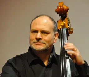 Ein Mann spielt einen Kontrabass auf einer Bühne. Er trägt ein schwarzes Hemd und schaut konzentriert.