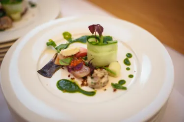 Ein kunstvoll angerichteter Teller mit verschiedenen Gemüse- und Fischzutaten. Grünes Pesto und frische Kräuter verleihen dem Gericht eine ansprechende Note.