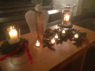 Ein dekorierter Tisch mit Kerzen, einem Holzengel und einer Weihnachtskranz. Die Atmosphäre ist festlich und gemütlich.