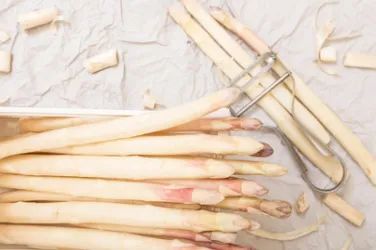 Frischer Spargel liegt auf einem Arbeitsbereich mit einem Schäler. Er ist hell und sauber, bereit zum Kochen.