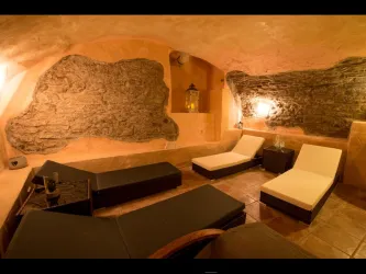 Ein gemütlicher Wellnessbereich mit Liegen und sanfter Beleuchtung. Die Wände sind aus natürlichem Stein und schaffen eine entspannende Atmosphäre.