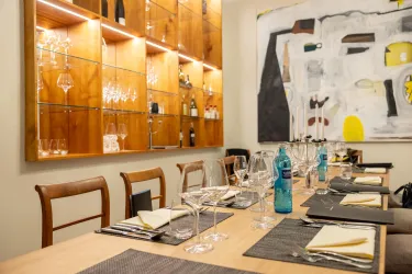 Ein elegantes Esszimmer mit einem Holztisch und schön eingedecktem Geschirr. Acuh eine Wand mit Gläsern und Flaschen sowie ein modernes Kunstwerk sind sichtbar.