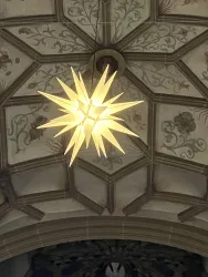 Eine leuchtende Sternenlampe hängt unter einer kunstvoll verzierten Decke. Die Decke zeigt florale Motive und geometrische Muster.