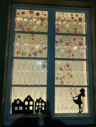 Ein Fenster mit bunten Sternen und einer Silhouette eines Mädchens. Im Vordergrund sind kleine Häuser zu sehen.