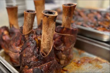 Ein rustikales Gericht mit mehreren großen Fleischstücken und langen Knochen. Die Oberfläche ist gut gebraten und zeigt eine appetitliche Farbe.