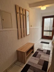 Ein heller Flur mit einem modernen Schuhregal und einer Spiegelwand. Die Tür zum Außenbereich lässt viel Licht herein.