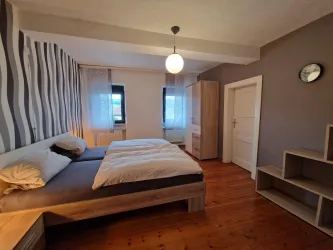 Ein gemütliches Schlafzimmer mit zwei Einzelbetten und einem Holzfußboden. Die Wände sind mit modernen Mustern dekoriert und es gibt viel natürliches Licht durch die Fenster.