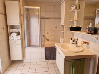 Ein helles Badezimmer mit einer Dusche und einem großen Waschbecken. Saubere Handtücher sind ordentlich in einem Regal gestapelt.