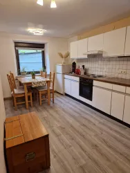 Eine helle Küche mit modernen Möbeln und einem Tisch für vier Personen. Die Wände sind hell und der Boden hat eine Holzoptik.