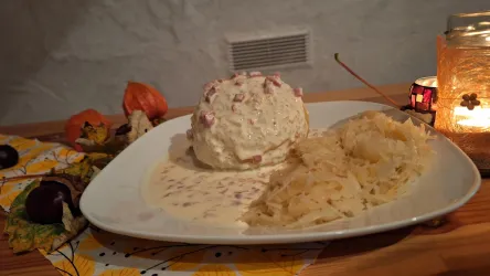 Ein Teller mit einem cremigen Gericht und Beilage aus Kartoffeln. Auf der Seite liegt etwas Sauerkraut, umgeben von herbstlicher Dekoration.