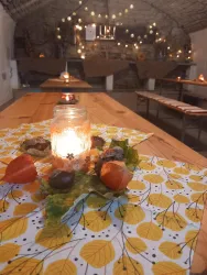 Ein gemütlicher Raum mit Holzstühlen und einem langen Tisch. Auf dem Tisch steht eine Kerze in einem Glas, umgeben von herbstlichen Dekorationen.