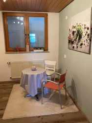 Ein gemütlicher Raum mit einem Tisch und zwei Stühlen. An der Wand hängt ein Bild mit bunten Motiven.