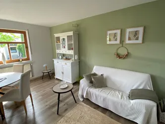 Ein einladendes Wohnzimmer mit einer gemütlichen Couch und einem stilvollen Sideboard. Die Wände sind in sanftem Grün gestrichen und es gibt viel natürliches Licht.
