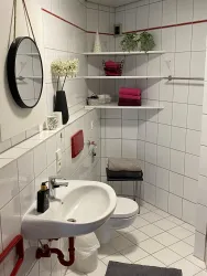 Ein modernes Badezimmer mit weißen Fliesen und einem runden Spiegel. Es gibt Handtücher in verschiedenen Farben und dekorative Pflanzen auf den Regalen.
