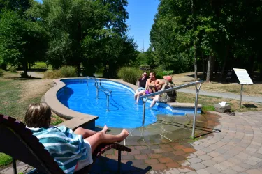 Eine entspannte Szene an der Kneippanlage mit mehreren Personen, die das Wasser genießen. Im Hintergrund sind Bäume und eine grüne Landschaft sichtbar.