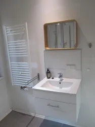 Ein modernes Badezimmer mit einem weißen Waschbecken und einem großen Spiegel. An der Wand hängt ein Handtuchwärmer und die Wände sind hell gestrichen.