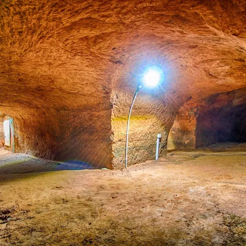 Eine weitläufige Höhle mit gewölbten Wänden und beleuchtetem Innenraum. Der Boden ist sandig und die Umgebung wirkt natürlich und unverarbeitet.