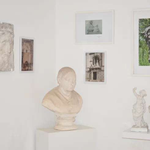 Ein Raum mit verschiedenen Skulpturen und Bildern an der Wand. Im Mittelpunkt steht eine weiße Büste einer Person auf einem einfachen Sockel.
