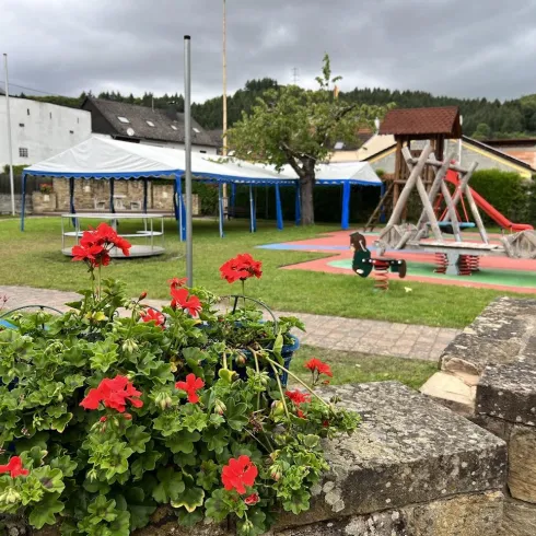 Ein schöner Spielplatz mit Rutsche und Schaukel. Im Vordergrund stehen blühende Geranien.