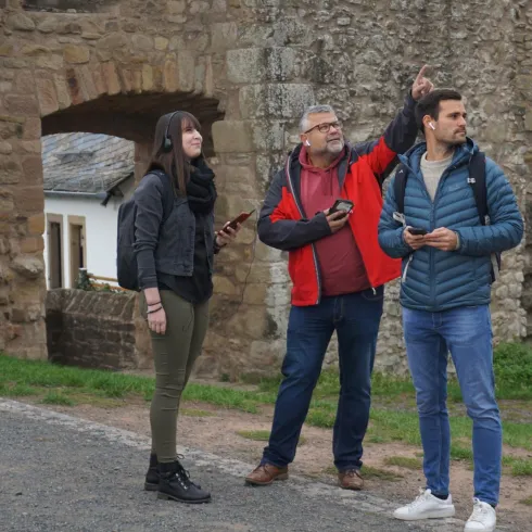 Drei Personen stehen vor einer historischen Ruine. Sie scheinen sich zu unterhalten und schauen in die gleiche Richtung.