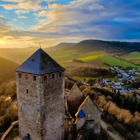 Eine alte Burg steht auf einem Hügel mit Blick auf malerische Landschaften. Die Sonne geht hinter den Bergen unter und sorgt für eine wundervolle Atmosphäre.
