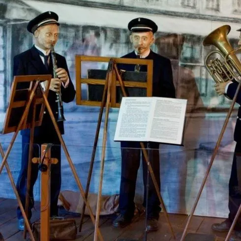 Eine Gruppe von Musikern in historischen Uniformen steht um Notenständer. Sie spielen traditionelle Instrumente wie Klarinette und Posaune.