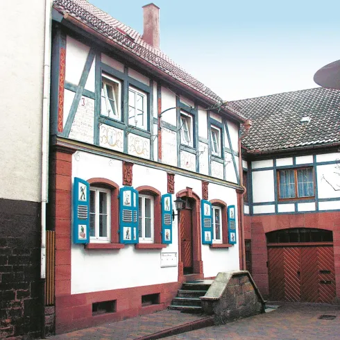 Ein historisches Fachwerkhaus mit blau gestrichenen Fensterläden. Die Fassade ist aus Holz und Stein und gibt der Umgebung einen charmanten Charakter.