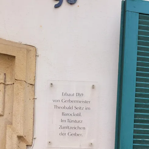 Historische Informationstafel am Eingang. Neben dem Briefkasten befindet sich ein QR-Code.