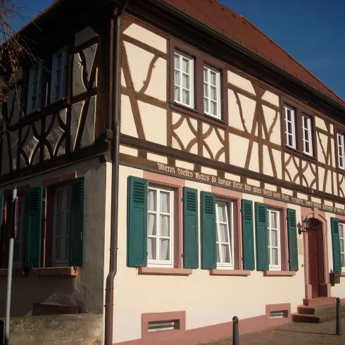 Ein traditionelles Fachwerkhaus mit bunten Fensterläden. Die Fassade zeigt ein charakteristisches Muster und ist von einem klaren blauen Himmel umgeben.