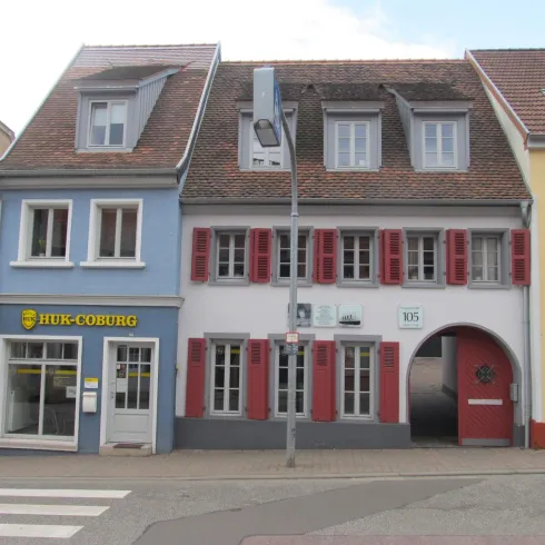 Das Bild zeigt eine malerische Straße mit mehreren historischen Gebäuden. Die Fassaden sind farbenfroh gestaltet, mit blauen und roten Akzenten.