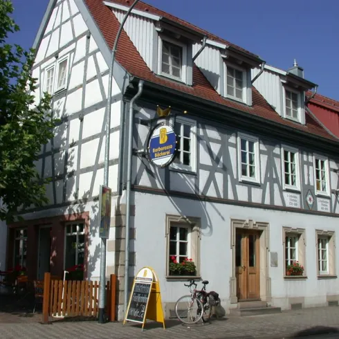 Ein charmantes Fachwerkhaus mit einem einladenden Restaurant im Erdgeschoss. Es stehen Fahrräder vor der Tür, und die Sonne scheint durch den klaren Himmel.