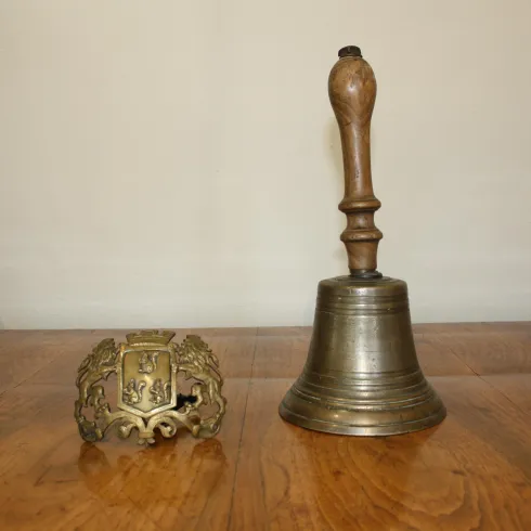 Eine metallene Glocke steht neben einem dekorativen, goldenen Objekt. Beide befinden sich auf einer Holzoberfläche.