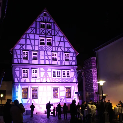 Ein historisches Fachwerkhaus erleuchtet in bunten Farben. Menschen versammeln sich in der Mitte der Straße.
