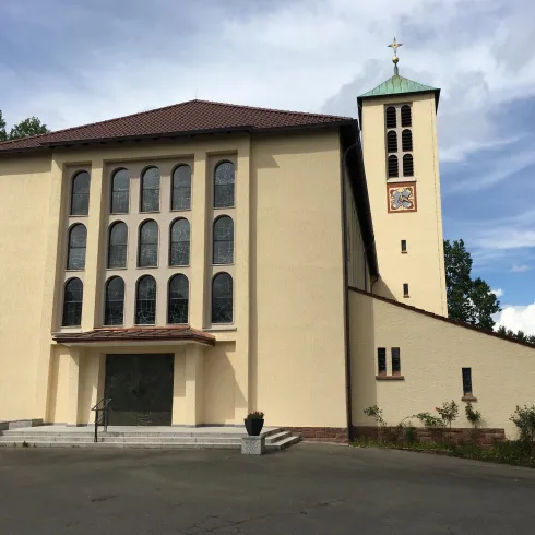 Ein modernes Kirchengebäude mit einer markanten Fassade und einem Uhrturm. Der Himmel ist klar und die Umgebung ist grün.