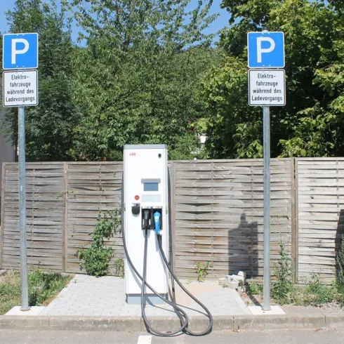 Eine Ladestation für Elektroautos steht auf einem Parkplatz. Daneben befinden sich zwei Schilder, die auf die Nutzung hinweisen.