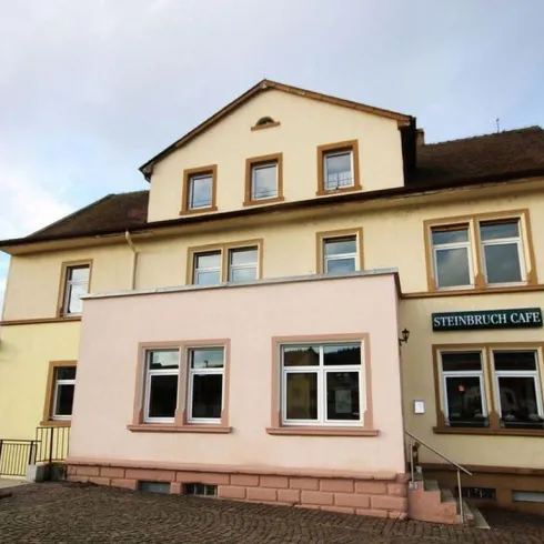 Ein großes Gebäude mit mehreren Fenstern und einem schönen Eingangsbereich. Das Steinenbruch Café ist an der Fassade deutlich zu sehen.