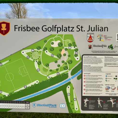 Eine Übersichtskarte des Frisbee Golfplatzes St. Julian mit verschiedenen Bahnen und einem Spielplatz. Der Platz befindet sich in einer grünen Umgebung entlang eines Flusses.