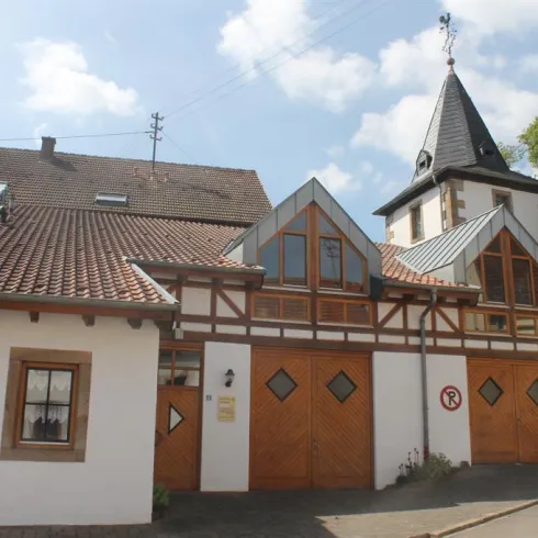 Ein traditionelles Fachwerkhaus mit einem modernen Anbau. Der Dachstuhl hat eine markante Form und die Fassade ist hell gestrichen.